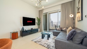 A modern living room with a flat-screen TV, a sofa, a coffee table, and a large window with curtains. - Zapbed House-DT 2103 (Dubai)