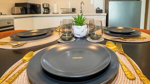 A dining table set with black plates, gold cutlery, and a small potted plant. - Zapbed House-DT 2103 (Dubai)
