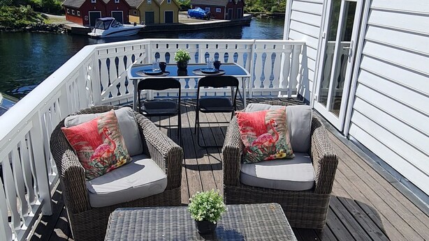Une terrasse dotée de meubles en osier, d’une petite table et offrant une vue sur les bateaux et les maisons de l’autre côté de l’eau.