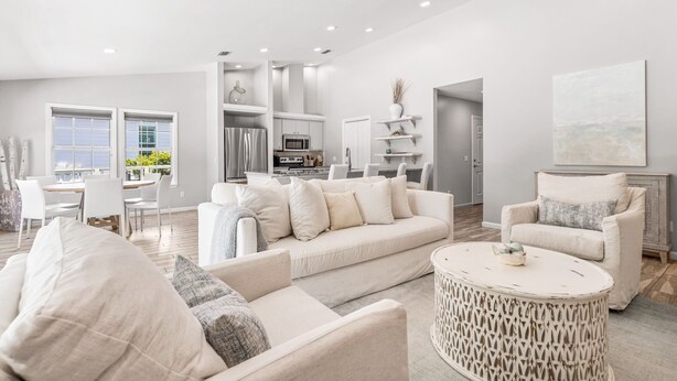 A spacious living room with a large white sofa, a round coffee table, and a dining area with a white table and chairs. - Dog-Friendly House with Private Pool (Santa Rosa Beach)