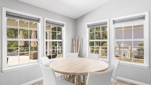 A dining area with a round table and four white chairs, large windows with white frames, and a view of the outdoors. - Dog-Friendly House with Private Pool (Santa Rosa Beach)