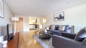 A modern living room with a grey sofa, a round coffee table, and a wooden TV stand. - Cosy 1 Bed Flat in Greenwich (London)