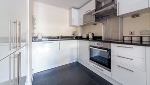 A modern kitchen with white cabinets, a black countertop, a built-in oven, and a microwave. - Cosy 1 Bed Flat in Greenwich (London)