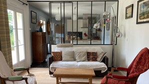 Een woonkamer met een bank, twee stoelen, een salontafel en een keuken die zichtbaar is via een glazen scheiding.