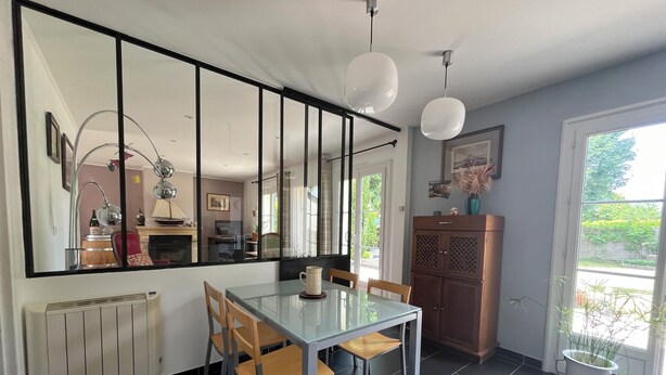 Een eethoek met een glazen tafel, houten stoelen, een witte karaf en een kast.