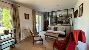 Een woonkamer met een bank, fauteuils, een salontafel, een eettafel en een keuken die zichtbaar is door een glazen scheiding.