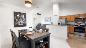 A modern kitchen with wooden cabinets, stainless steel appliances, and a dining area with a dark wooden table and chairs.