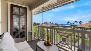 A balcony with a view of the ocean, a wooden door, and a small table with fruits.