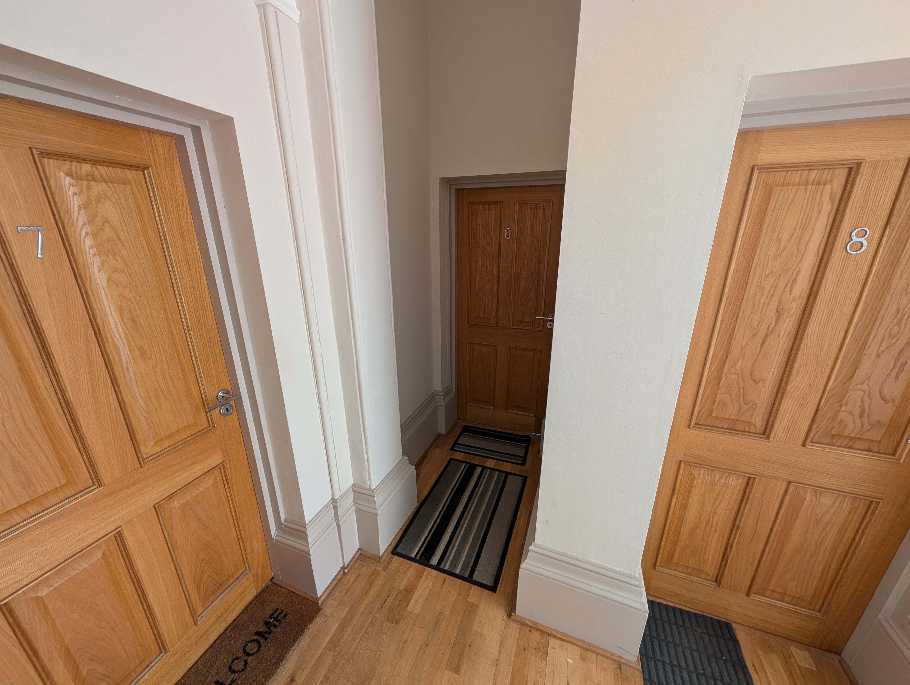 Un pasillo con puertas de madera numeradas 7 y 8, una alfombra de bienvenida y un felpudo.