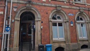 A red brick building with arched windows and a black gate. There are two trash bins on the sidewalk.