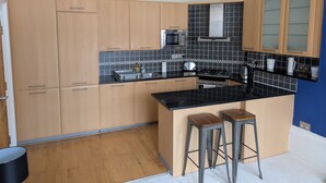 A modern kitchen with wooden cabinets, a black countertop, a microwave, a stove, and two stools.