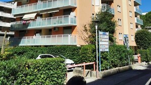 A multi-story residential building with balconies, a parking area, and a signboard.