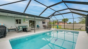 A covered outdoor swimming pool with a patio area, a grill, and a pool table.