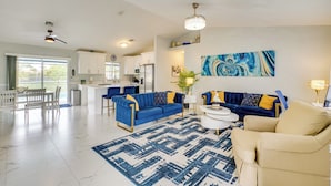 A spacious living area with a blue sofa set, a beige armchair, and a dining table with chairs.