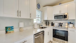 A modern kitchen with white cabinets, stainless steel appliances, a dishwasher, and a decorative painting.