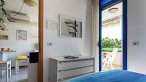 Ein Schlafzimmer mit einem Bett, einem Schreibtisch und einem Stuhl. Ein Fenster bietet Blick auf Grünfläche.