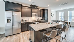 A modern kitchen with dark cabinetry, stainless steel appliances, and a granite countertop island with bar stools. - Walk to Music Factory: Townhome w/ Rooftop Deck! (Charlotte)