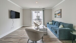 A living room with a sofa, armchair, and coffee table. There is a TV mounted on the wall and a painting on the wall. - Walk to Music Factory: Townhome w/ Rooftop Deck! (Charlotte)