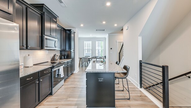 A modern kitchen with dark cabinetry, a stainless steel refrigerator, and a central island. - Walk to Music Factory: Townhome w/ Rooftop Deck! (Charlotte)