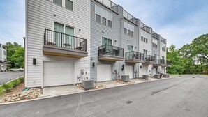 A multi-story residential building with a row of garage doors, outdoor air conditioning units, and balconies with black railings. - Walk to Music Factory: Townhome w/ Rooftop Deck! (Charlotte)