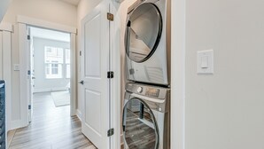 A laundry room with two stacked washers and dryers, a wooden floor, and a door leading to another room. - Walk to Music Factory: Townhome w/ Rooftop Deck! (Charlotte)