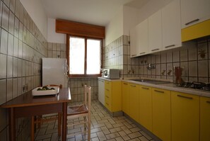 Eine Küche mit gelben Schränken, einem weißen Kühlschrank, einem Fenster mit Holzjalousie und einer gefliesten Spritzschutzwand.