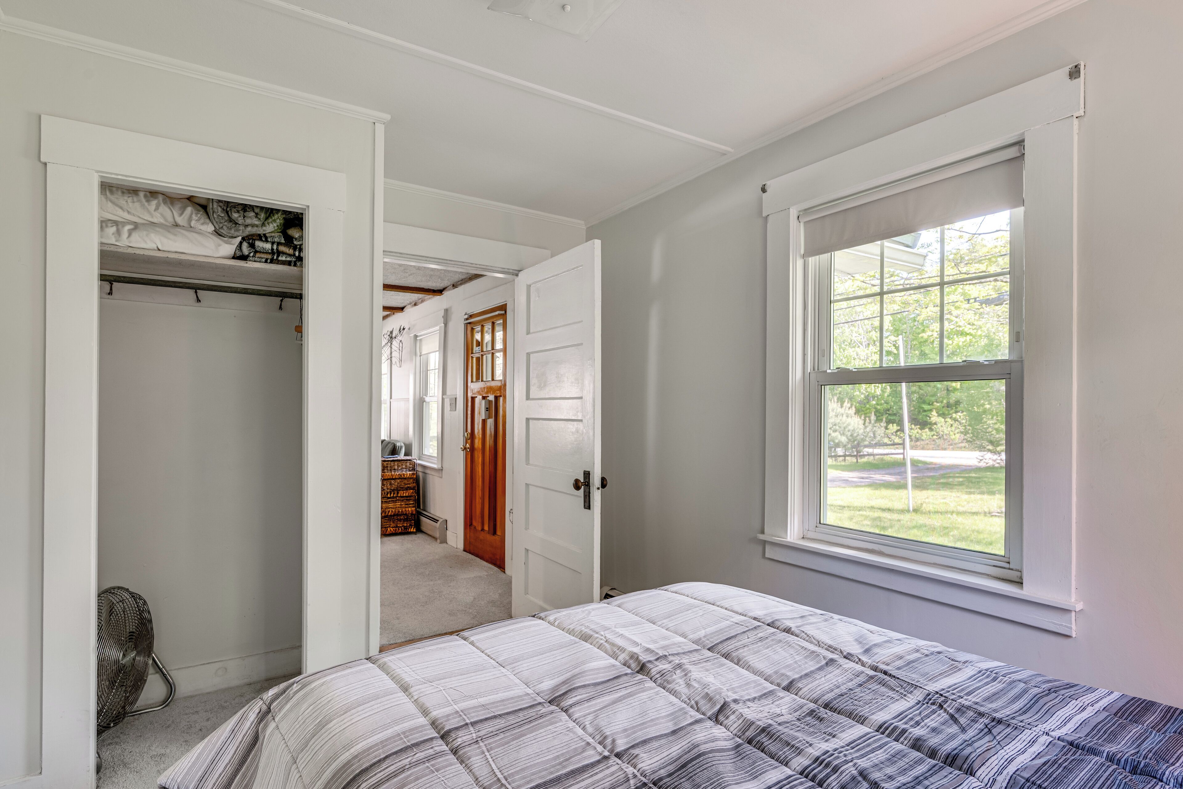 Un dormitorio con una cama, un armario, una ventana y una puerta que da a otra habitación.