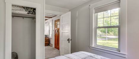Un dormitorio con una cama, un armario, una ventana y una puerta que da a otra habitación.