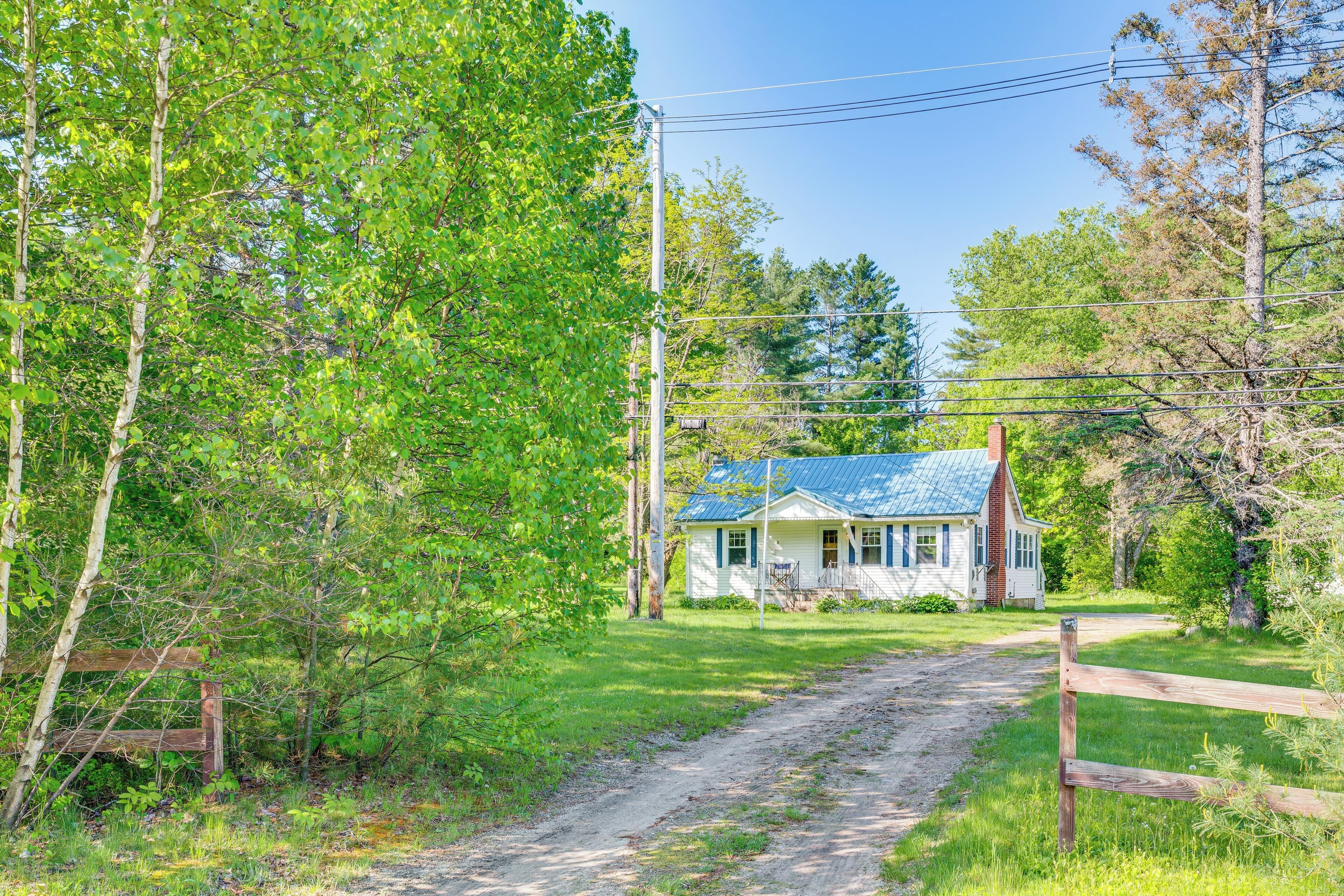 A rustic house with a dirt path leading to it, surrounded by lush greenery and trees.