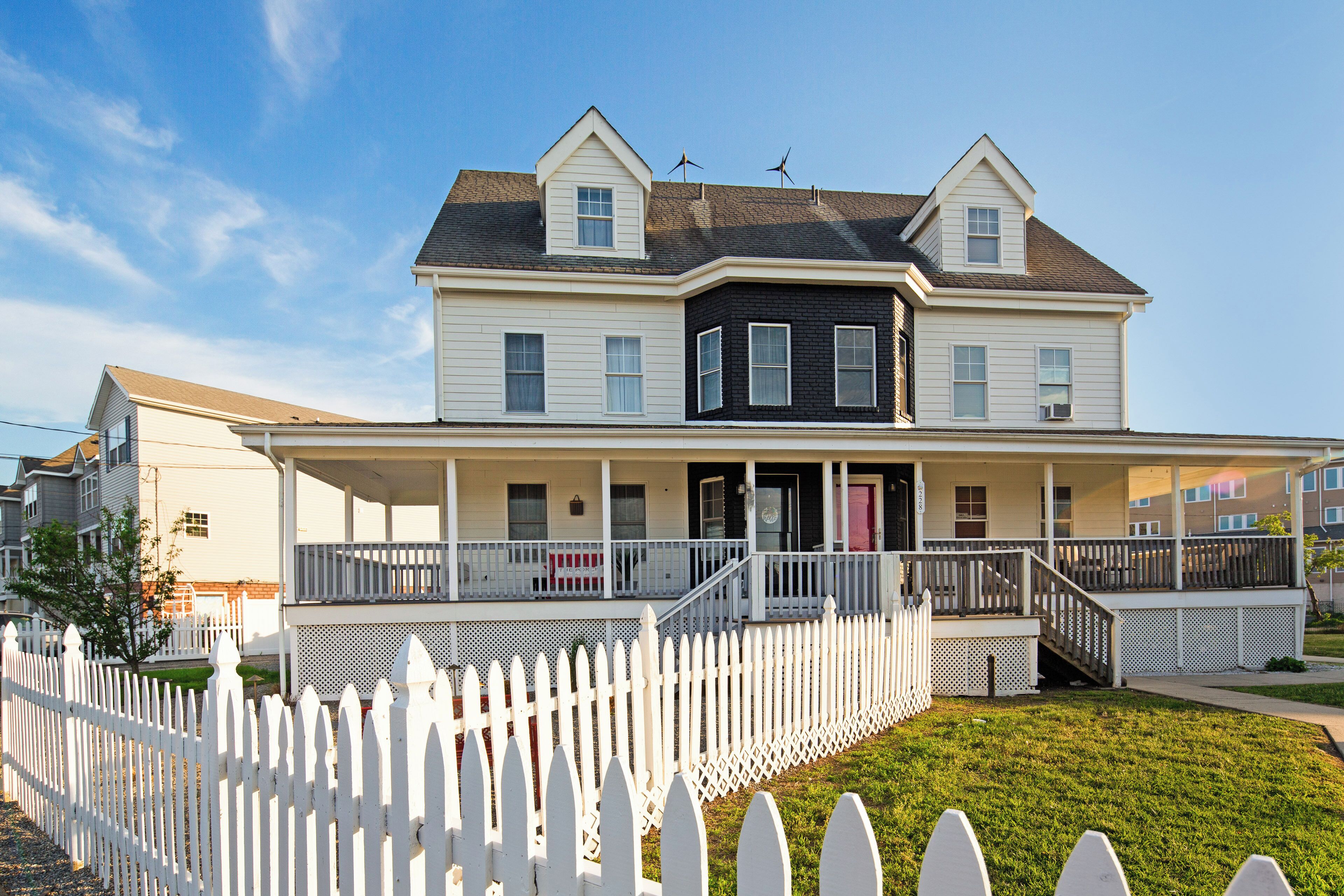 A two-story house with a porch, a white picket fence, and a clear sky.