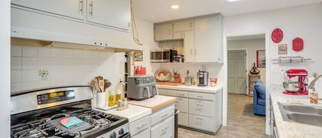A modern kitchen with white cabinets, a gas stove, a microwave, and a coffee maker.