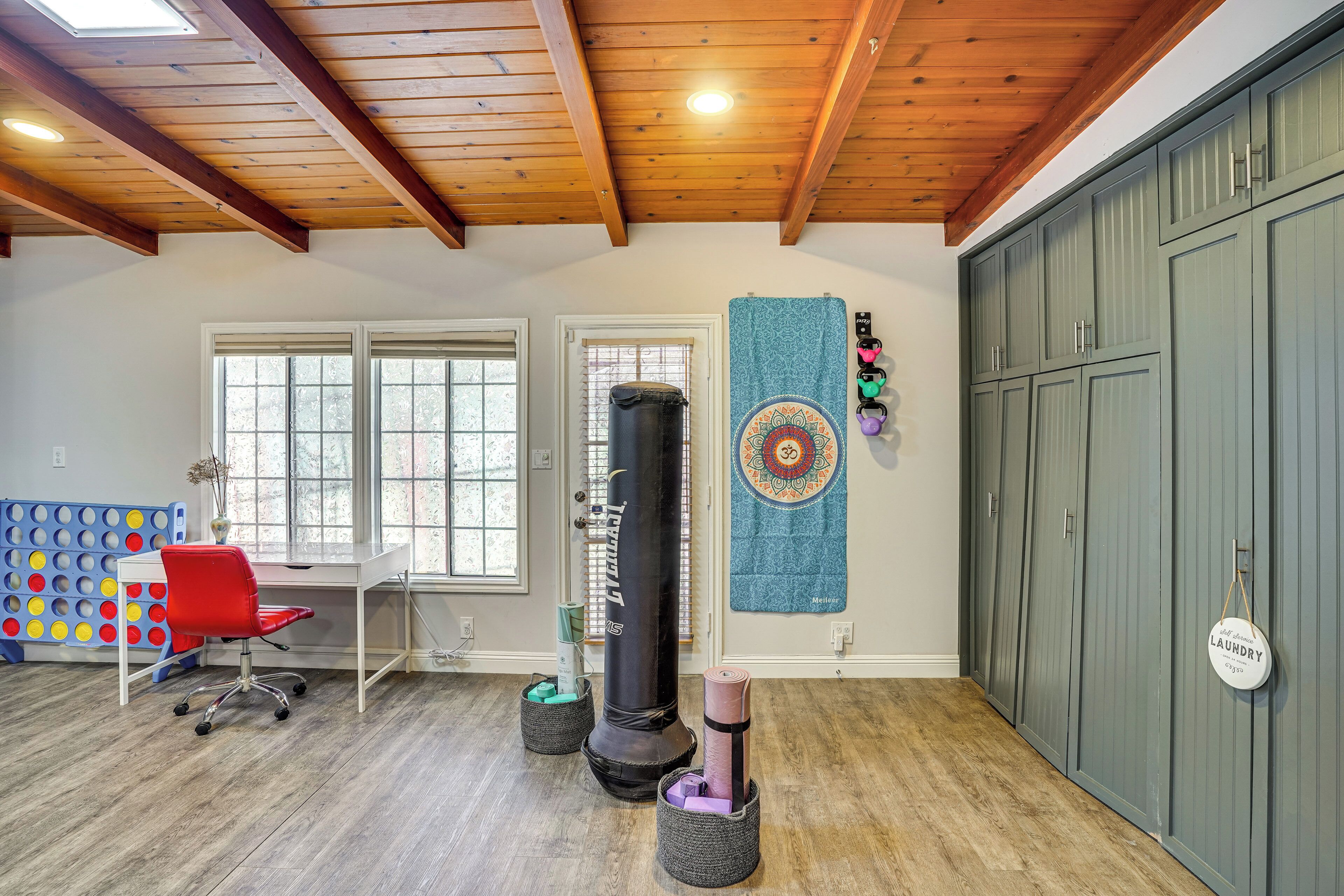 A room with a wooden ceiling, a punching bag, a red office chair, a desk, and a large grey wardrobe.