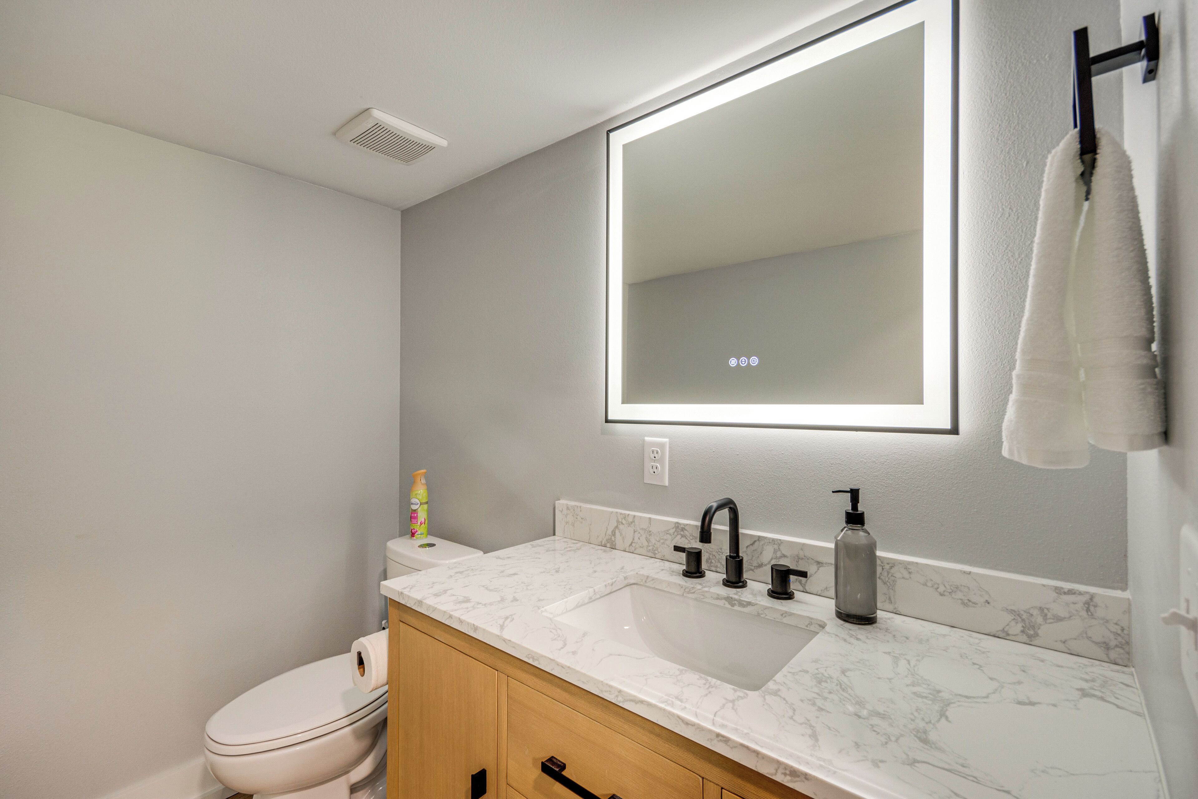 A bathroom with a white toilet, a sink with a marble countertop, a mirror, and a towel rack.