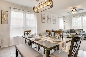A dining area with a wooden table set for six, surrounded by chairs, a ceiling fan, and artwork on the walls.
