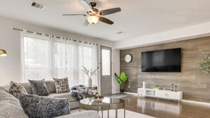 A modern living room with a sofa, coffee table, and a flat-screen TV mounted on a wooden wall. - Golf, Bike, Fish & More: Family Getaway in Katy (Katy)