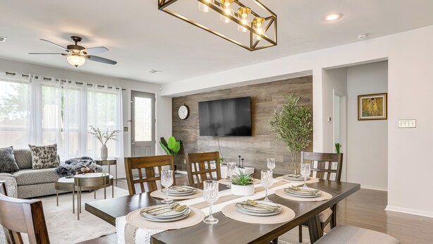 A modern dining area with a wooden table set for six, surrounded by chairs. A ceiling fan and a mounted TV are visible. - Golf, Bike, Fish & More: Family Getaway in Katy (Katy)