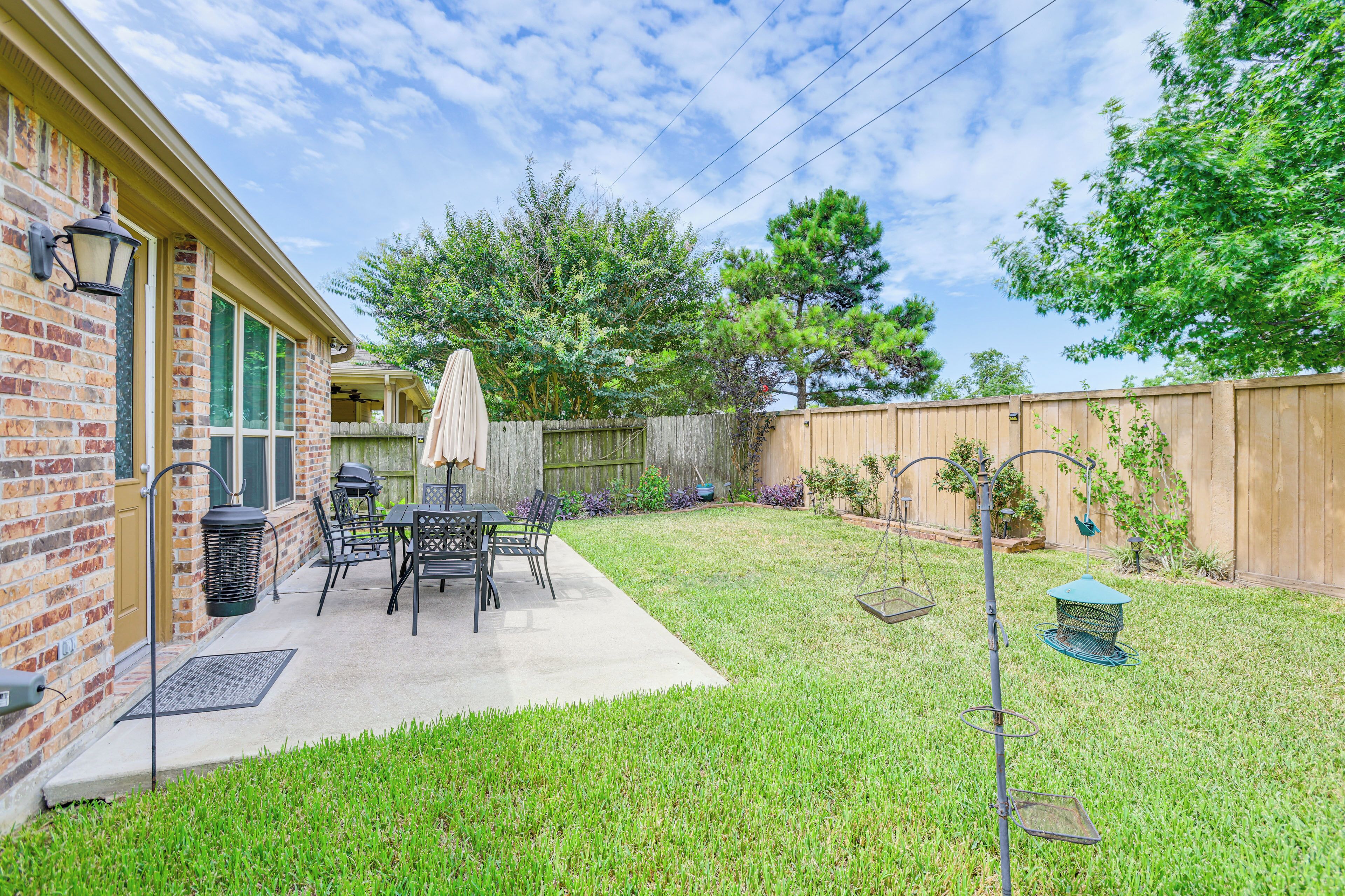 A backyard with a patio, a brick house, a wooden fence, and a lawn.
