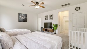 A bedroom with two beds, a ceiling fan, a TV, and a crib. - Golf, Bike, Fish & More: Family Getaway in Katy (Katy)