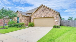 A two-story brick house with a beige garage door, a front yard with grass and shrubs, and a wooden fence in the background. - Golf, Bike, Fish & More: Family Getaway in Katy (Katy)