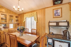 Una cocina con paneles de madera, una mesa de comedor, sillas, una estufa y un ventanal con cortinas.