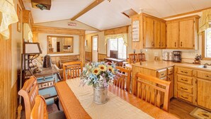 Une cuisine avec des meubles de rangement en bois, une table à manger avec des chaises, une cuisinière et un vase rempli de fleurs.