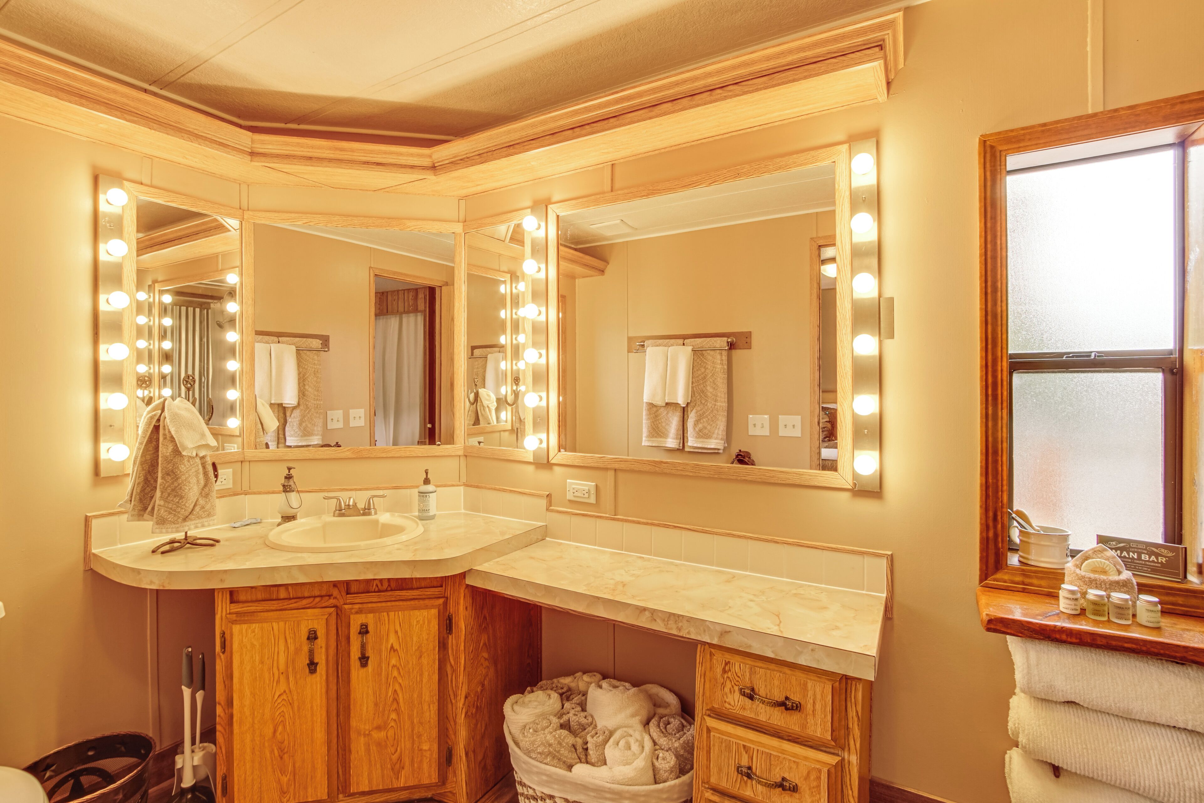 A bathroom with a vanity, mirrors, and a sink. There are towels and toiletries visible.