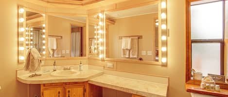A bathroom with a vanity, mirrors, and a sink. There are towels and toiletries visible.
