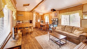 Un vaste espace de vie doté d’un plancher en bois, d’un canapé, d’une table basse et d’une table à manger avec des chaises. Il y a également un coin cuisine avec des armoires en bois et un réfrigérateur.