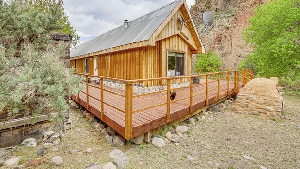 Une cabane en bois avec un toit en métal, une terrasse en bois et des fondations en pierre.