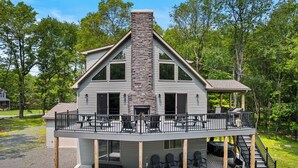 A two-story house with a stone fireplace, a covered deck with outdoor seating, and a staircase leading to an upper level. - Hot Tub & Community Beach: Albrightsville Home! (Albrightsville)