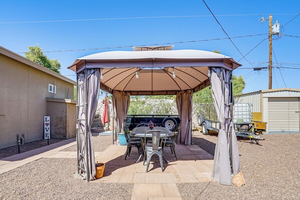 Une terrasse couverte avec une table et des chaises, une pancarte sur laquelle on peut lire « AMOUR », et un véhicule à l’arrière-plan.