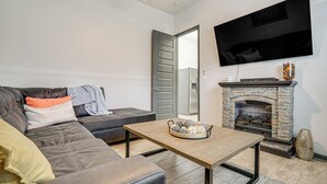 Un salon moderne avec un canapé en cuir, une table basse en bois, une cheminée en pierre et un téléviseur à écran plat fixé au mur.