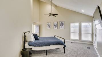 A bedroom with a bed, a ceiling fan, and three wall-mounted pictures.