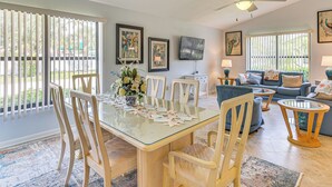 A spacious living area with a dining table, chairs, a sofa, and a TV mounted on the wall. - 5 Mi to Fort Myers Beach: Home w/ Large Yard! (Fort Myers)
